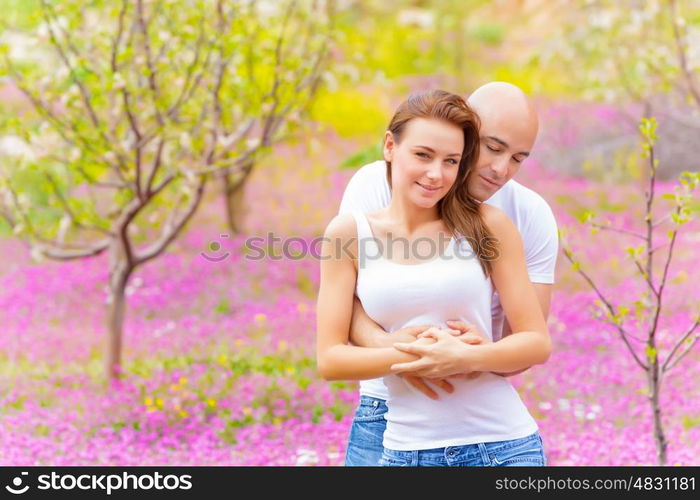 Happy young couple hugging in spring park, enjoying each other, springtime nature, purple flowers, tenderness and love concept