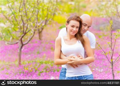 Happy young couple hugging in spring park, enjoying each other, springtime nature, purple flowers, tenderness and love concept