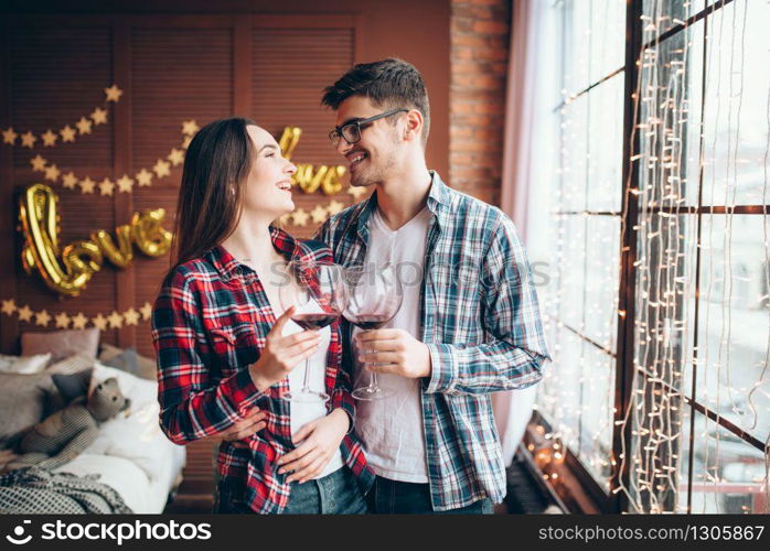 Happy young couple hugs together against large window from floor. Man and woman embrace, romantic relationship. Young couple hugs against large window from floor