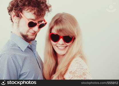 Happy young couple in heart shaped glasses. Smiling friends woman and man in studio.