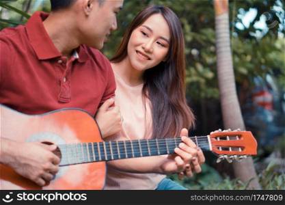 Happy young couple in love sitting in the garden and playing guitar and singing. Concept of Memorable and impressive moments