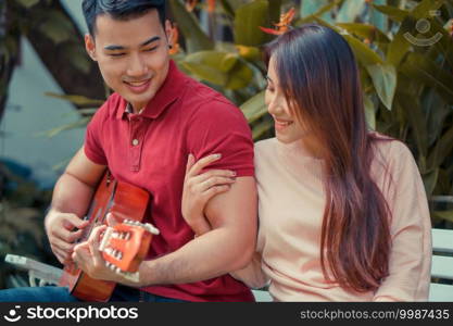 Happy young couple in love sitting in the garden and playing guitar and singing. Concept of Memorable and impressive moments
