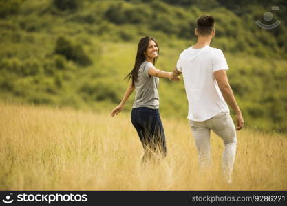 Happy young couple in love walking through grass field on a summer day