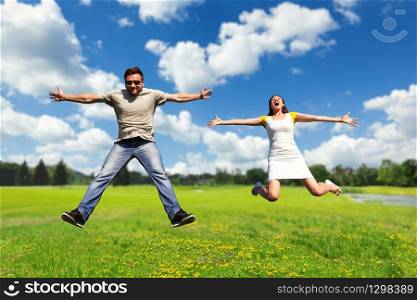 Happy young couple jumping high on the summer meadow. Couple having fun on the meadow