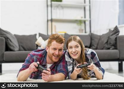 happy young couple lying carpet playing video game with joystick