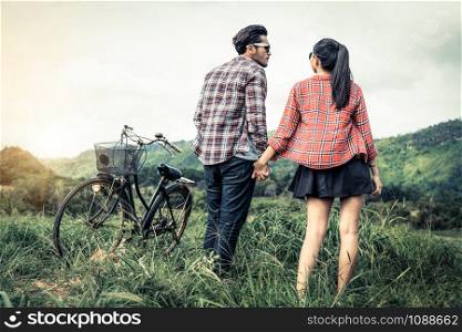 Happy young couple of man and woman ride bicycle at green grass field on the hills. Love and travel lifestyle concept.