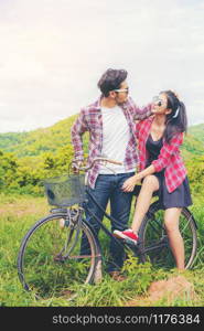 Happy young couple of man and woman ride bicycle at green grass field on the hills. Love and travel lifestyle concept.