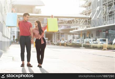 Happy young couple of shoppers walking in the shopping street towards and holding colorful shopping bags in hand. Concept of sale and black friday shopping
