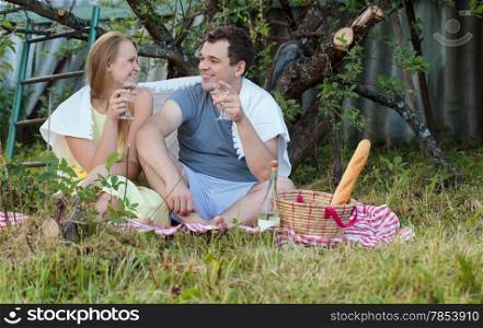 Happy young couple on picnic in the country. They sitting on the grass with glasses of wine covered with blanket. Romantic moments together