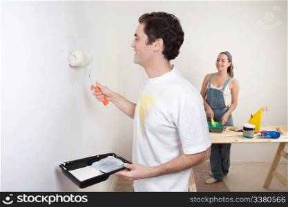 Happy young couple painting the wall white