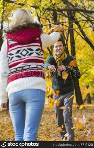 Happy young couple playing with autumn leaves in park