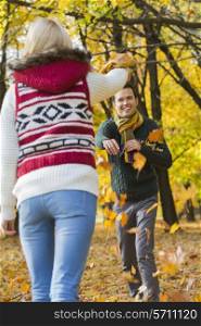 Happy young couple playing with autumn leaves in park
