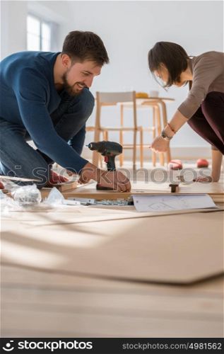 Happy young couple putting together self assembly furniture as they move into their new house.
