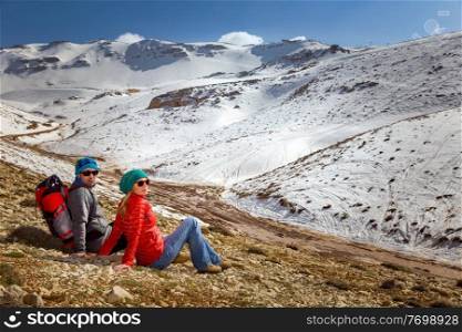 Happy Young Couple Sitting and Resting in the Mountains at the Base C&. Enjoying Adventure Hike in the Beautiful Snowy Mountains. Active Sportive Lifestyle. Winter Holidays Concept.