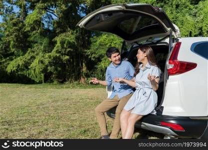happy young couple sitting and talking in open car back