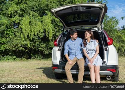 happy young couple sitting in open car back