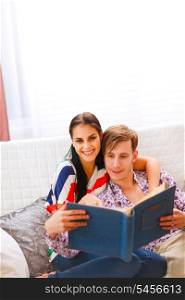Happy young couple sitting on couch and looking photo album &#xA;