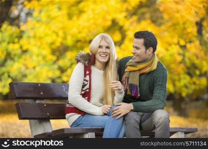 Happy young couple sitting on park bench during autumn