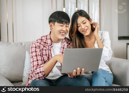 Happy Young couple sitting on sofa in living room at home use laptop computer working, talking and smile together with happiness, happy family concept