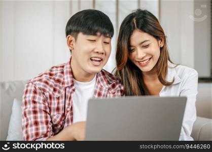 Happy Young couple sitting on sofa in living room at home use laptop computer working, talking and smile together with happiness, happy family concept