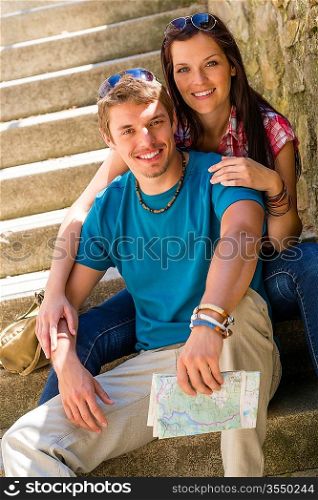Happy young couple sitting on stairs smiling holding city map
