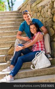 Happy young couple sitting on stone stairs smiling together outdoors