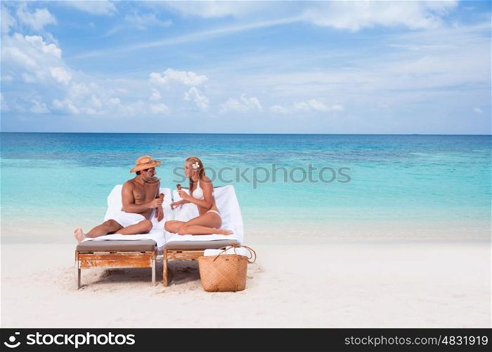 Happy young couple sitting on sunbed on the beach, eating tasty sweet cold ice cream, enjoying romantic summer vacation&#xA;