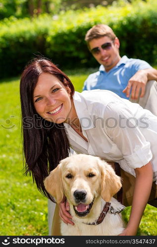 Happy young couple sitting with golden retriever dog in park