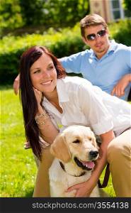 Happy young couple sitting with golden retriever dog in park