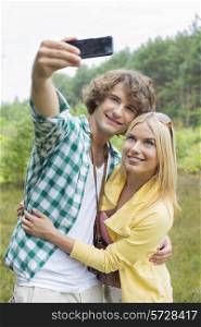 Happy young couple taking self portrait through cell phone in field