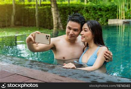 happy young couple taking selfie photo at edge of swimming pool