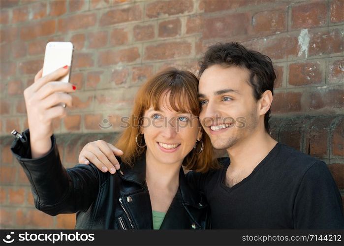 Happy young couple taking selfie with mobile phone in the city. Fun concept.