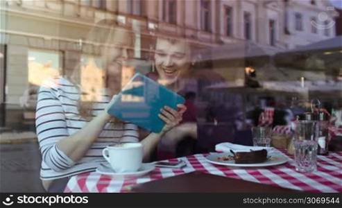 Happy young couple using touchpad in a cafe. View through the glass with city reflection