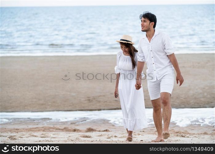 Happy young couple walking on the beach during honeymoon travel vacation.. Happy young couple walk on the beach on honeymoon.