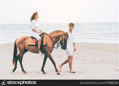 Happy young couple walking on the beach during honeymoon travel vacation.. Young couple goes horse riding on tropical beach.