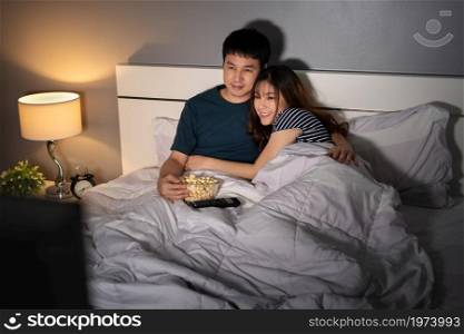 happy young couple watching TV on a bed at night