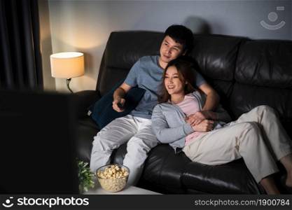 happy young couple watching TV on sofa at night