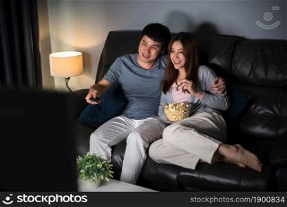 happy young couple watching TV on sofa at night