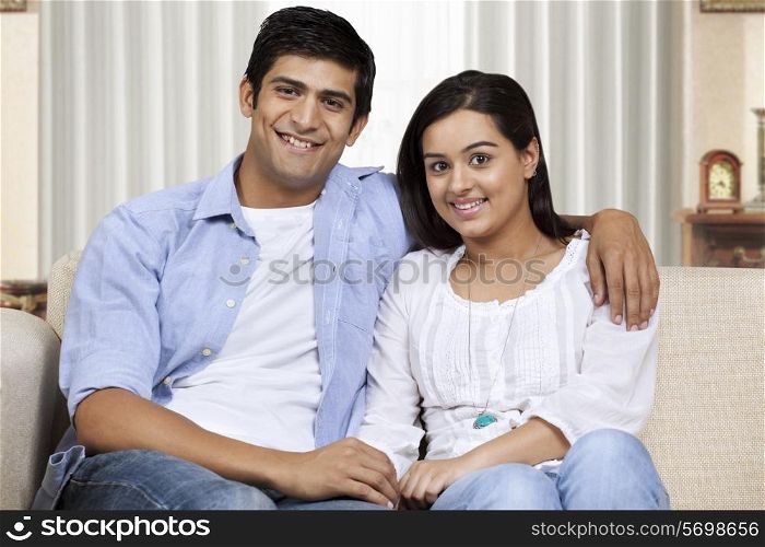 Happy young couple with arm around sitting on sofa