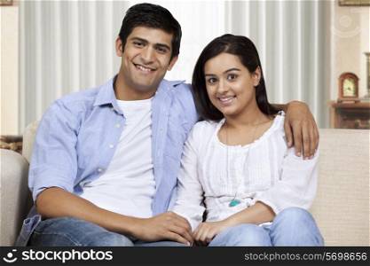 Happy young couple with arm around sitting on sofa