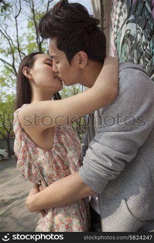 Happy young couple with arms around each other kissing by a wall with graffiti