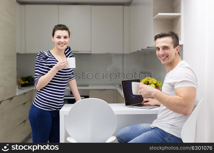 happy young couple with laptop computer enjoying morning coffee in modern kitchen at home