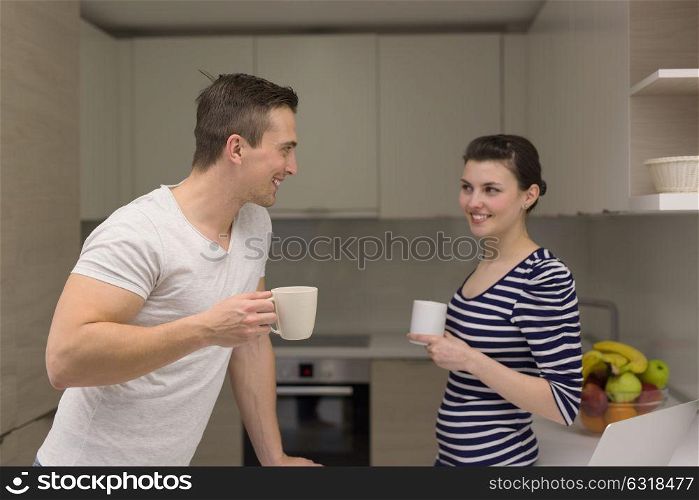 happy young couple with laptop computer enjoying morning coffee in modern kitchen at home