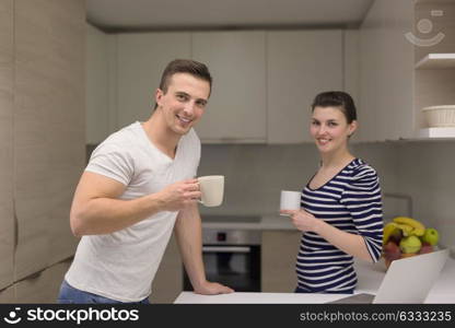 happy young couple with laptop computer enjoying morning coffee in modern kitchen at home