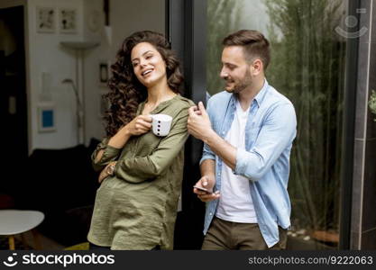 Happy young cute couple in love embracing each other and drinking coffee at home by the window