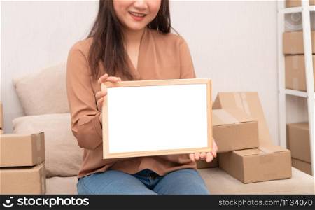 Happy young entrepreneur, sitting on the sofa and holding blank board for text and information. Concept of small business owner and Space for advertisement.