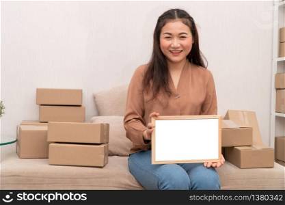 Happy young entrepreneur, sitting on the sofa and holding blank board for text and information. Concept of small business owner and Space for advertisement.