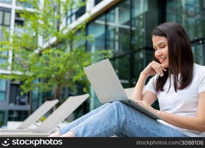 Happy young entrepreneur woman sitting on tanning bed beside pool and using laptop computer for remote online working digital, online business project in quiet yard of resort house, Work on vacation