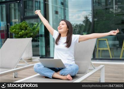 Happy young entrepreneur woman sitting on tanning bed beside pool and using laptop computer for remote online working digital, online business project in quiet yard of resort house, Work on vacation