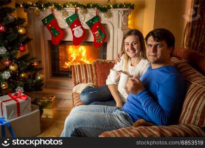 Happy young family drinking tea on sofa at fireplace